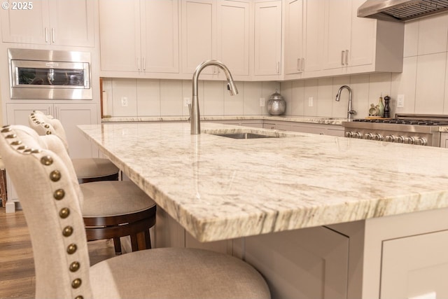 kitchen featuring decorative backsplash, a kitchen breakfast bar, oven, range hood, and a sink