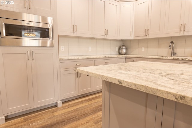 kitchen with white cabinets, stainless steel microwave, light stone counters, light wood-style floors, and a sink