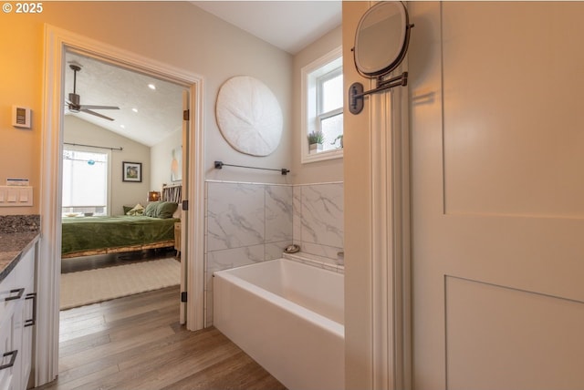 ensuite bathroom featuring ensuite bath, wood finished floors, vaulted ceiling, vanity, and a bath