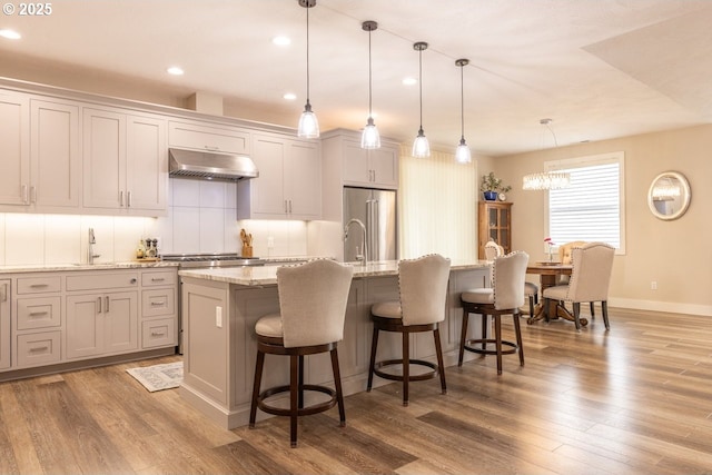 kitchen featuring stainless steel appliances, a kitchen island with sink, under cabinet range hood, and wood finished floors