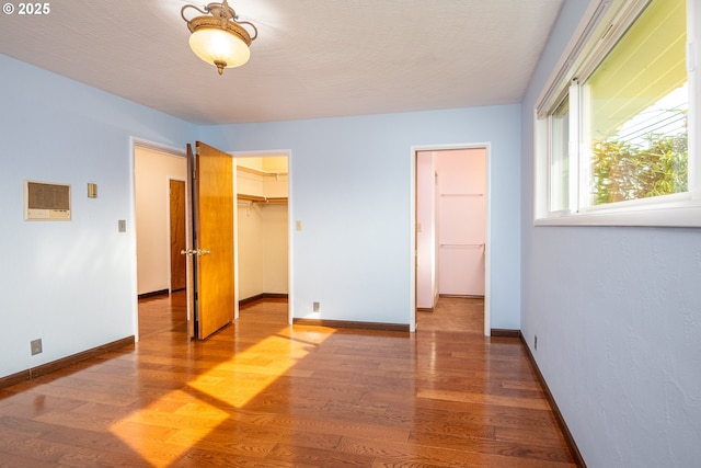 unfurnished bedroom featuring hardwood / wood-style flooring, a spacious closet, a closet, and a textured ceiling