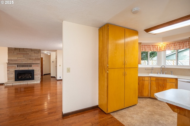 kitchen featuring a stone fireplace, sink, light hardwood / wood-style flooring, a textured ceiling, and dishwasher