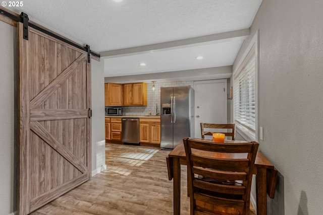 kitchen featuring backsplash, stainless steel appliances, a barn door, a textured ceiling, and light hardwood / wood-style flooring