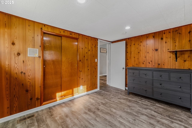 unfurnished bedroom with hardwood / wood-style flooring, a closet, and wood walls