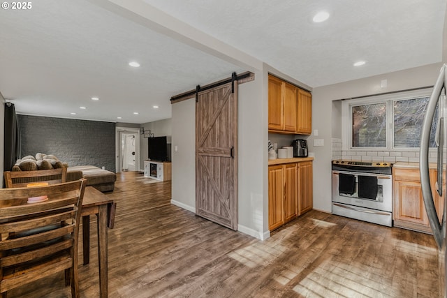 kitchen with a barn door, hardwood / wood-style floors, stainless steel range with electric cooktop, and decorative backsplash