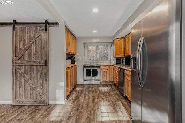 kitchen with stainless steel appliances, a barn door, dark hardwood / wood-style flooring, and backsplash