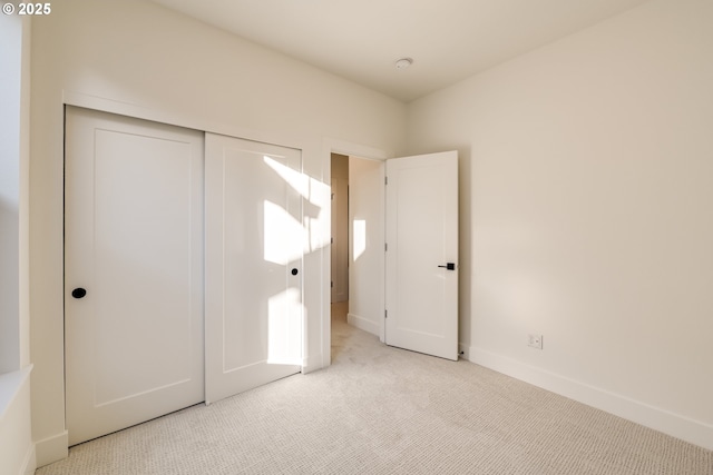 unfurnished bedroom with a closet, light carpet, and baseboards