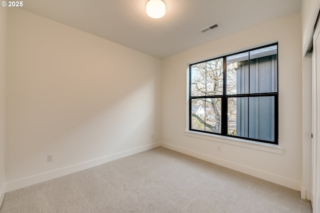 carpeted spare room with visible vents, baseboards, and a textured ceiling