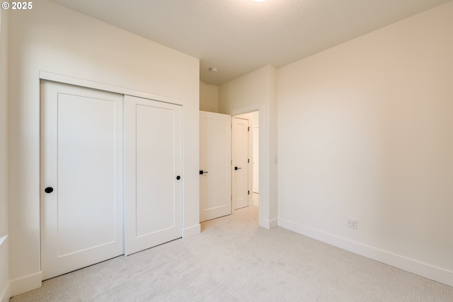 unfurnished bedroom with a closet, light colored carpet, and baseboards