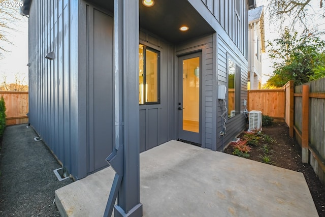 view of exterior entry featuring board and batten siding, a patio area, fence, and cooling unit