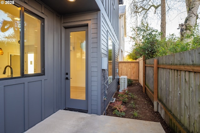 view of exterior entry featuring board and batten siding, a patio area, central AC, fence, and a sink