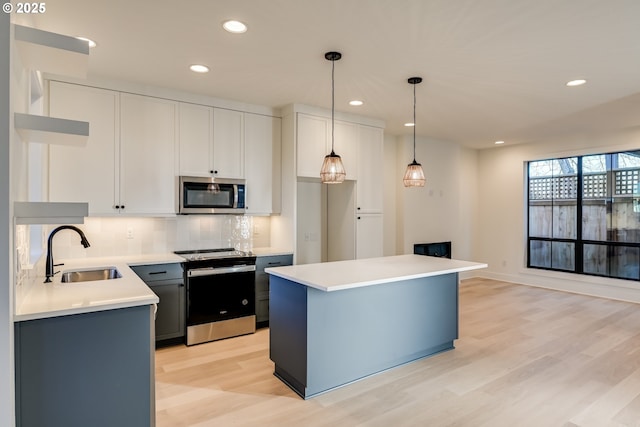 kitchen featuring appliances with stainless steel finishes, a center island, light countertops, white cabinetry, and a sink