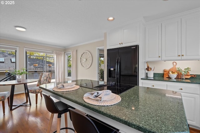 31560 SW Arbor Glen Loop, Wilsonville, OR 97070 - kitchen with wood finished floors, a breakfast bar, a textured ceiling, white cabinetry, and black appliances