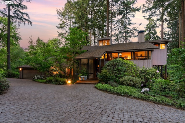 mid-century inspired home featuring a garage, a chimney, and decorative driveway