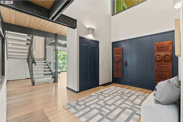 foyer with light wood-style floors, stairs, beam ceiling, and a towering ceiling