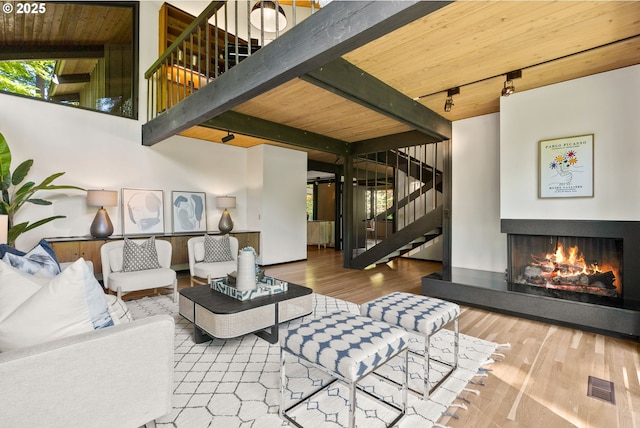 living room with stairs, beamed ceiling, track lighting, a warm lit fireplace, and wood finished floors