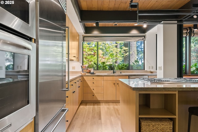 kitchen with stainless steel appliances, light brown cabinetry, light wood-style floors, a sink, and light stone countertops