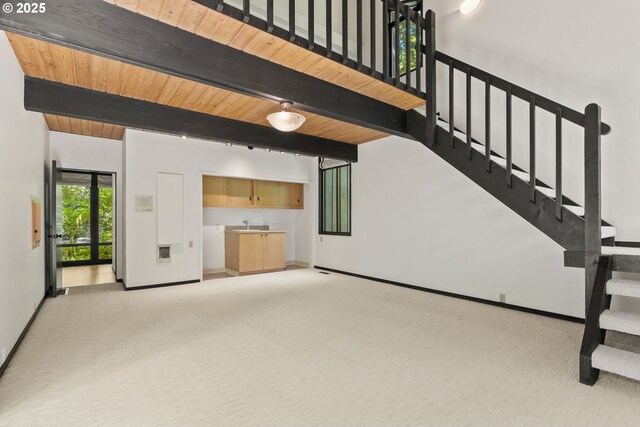 unfurnished living room with beamed ceiling, light carpet, stairway, baseboards, and wet bar