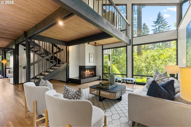 living area featuring stairway, wooden ceiling, wood finished floors, beam ceiling, and a multi sided fireplace