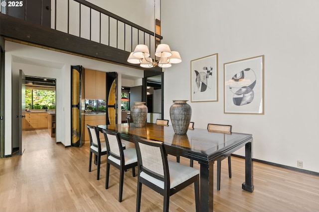 dining room featuring light wood finished floors, a high ceiling, a chandelier, and baseboards