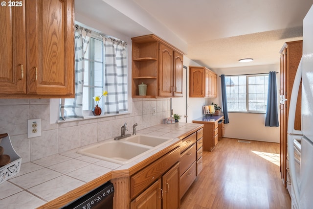 kitchen featuring a sink, tile counters, brown cabinets, light wood-style flooring, and open shelves