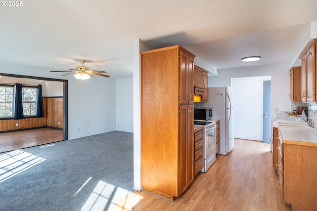 kitchen featuring white appliances, ceiling fan, a sink, tile counters, and a textured ceiling