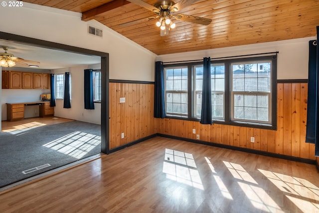 unfurnished room with visible vents, vaulted ceiling with beams, ceiling fan, wood walls, and light wood-style floors