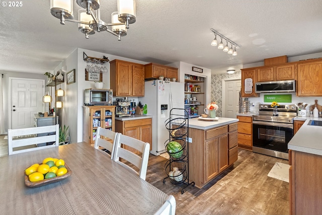 kitchen with light countertops, a textured ceiling, brown cabinetry, light wood-style flooring, and stainless steel appliances