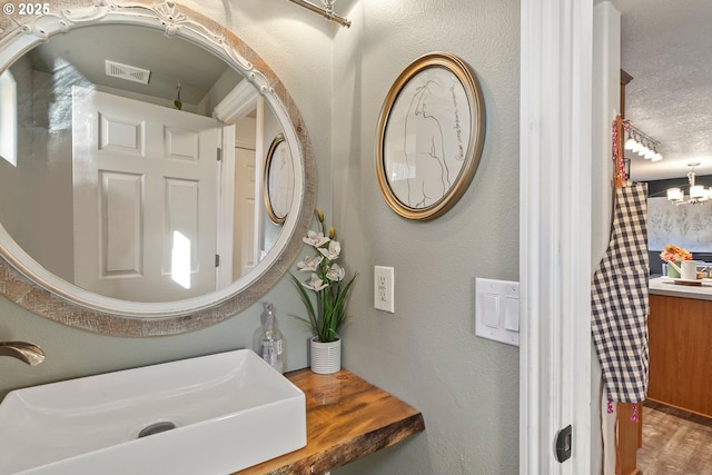 full bath with visible vents, a textured wall, wood finished floors, a chandelier, and a sink