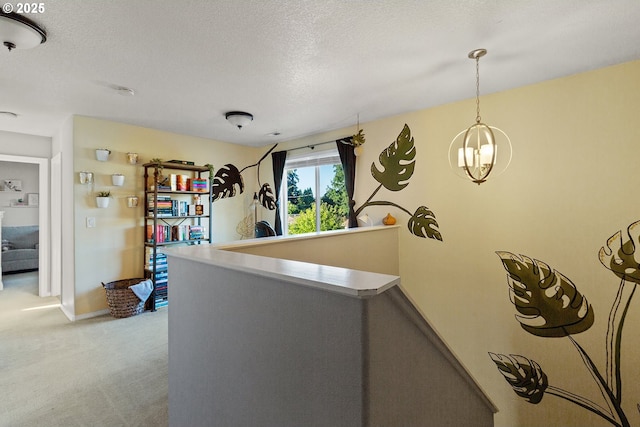 corridor featuring light carpet, a chandelier, a textured ceiling, and an upstairs landing