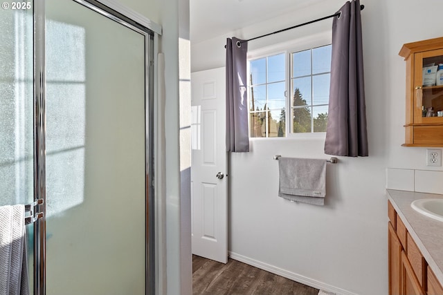 bathroom with vanity, baseboards, a shower with shower door, and wood finished floors