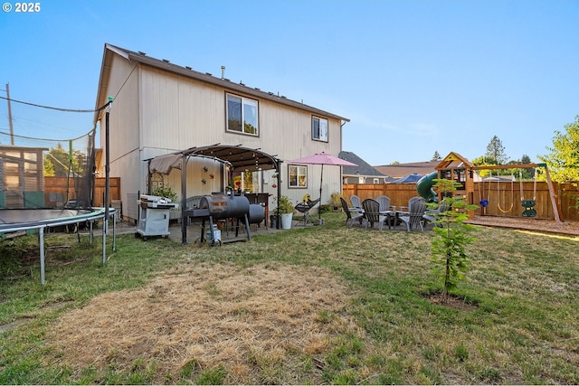 rear view of property featuring a fenced backyard, a yard, a trampoline, and a playground