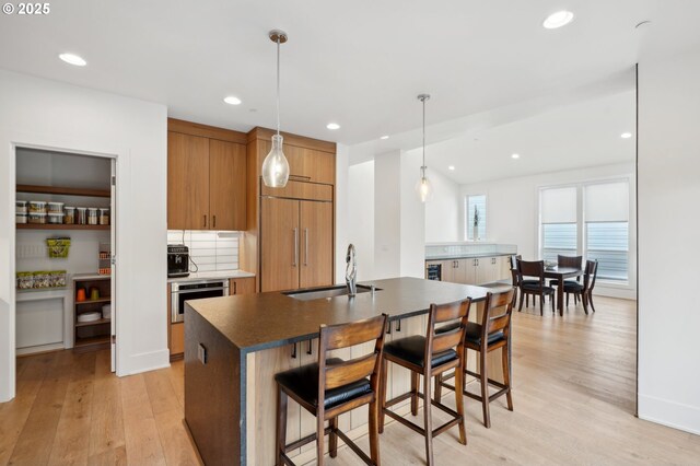 kitchen featuring paneled refrigerator, stainless steel oven, a sink, dark countertops, and light wood finished floors