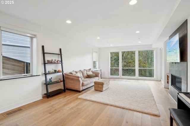 living area featuring light wood finished floors, recessed lighting, a tiled fireplace, and baseboards