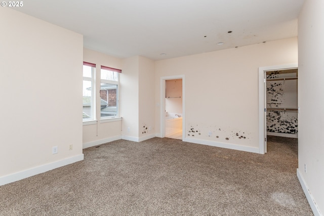 unfurnished bedroom with carpet, a walk in closet, and baseboards