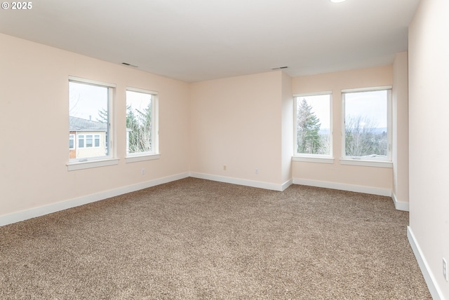 carpeted spare room featuring a healthy amount of sunlight, visible vents, and baseboards