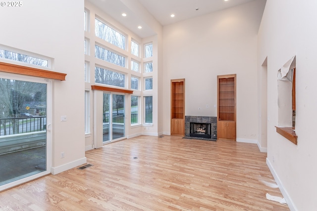 unfurnished living room featuring a wealth of natural light, a tiled fireplace, visible vents, and wood finished floors