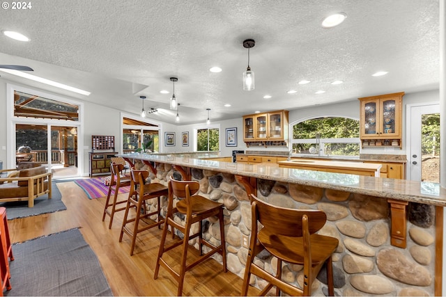 kitchen with a breakfast bar area, brown cabinetry, light wood finished floors, lofted ceiling, and glass insert cabinets