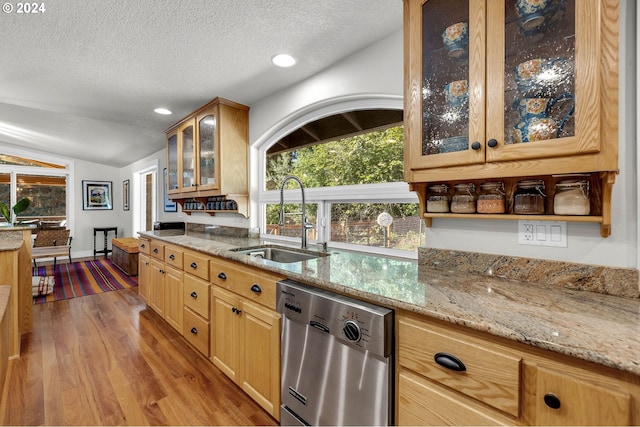 kitchen with a sink, light stone counters, stainless steel dishwasher, wood finished floors, and vaulted ceiling