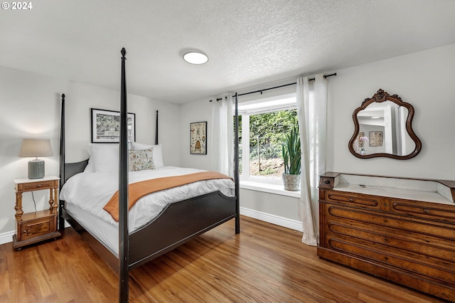 bedroom featuring baseboards, a textured ceiling, and wood finished floors