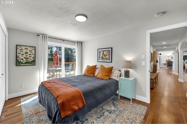 bedroom featuring hardwood / wood-style floors, access to exterior, baseboards, and a textured ceiling