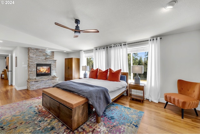 bedroom with light wood-type flooring, baseboards, a textured ceiling, and a stone fireplace