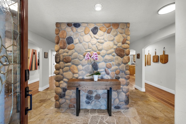 interior details featuring arched walkways, a textured ceiling, and baseboards