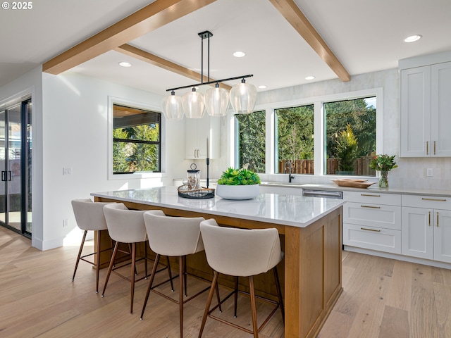 kitchen with light wood-type flooring, beamed ceiling, light stone counters, a center island, and a breakfast bar area