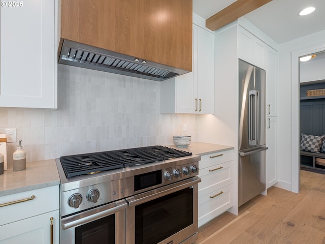 kitchen featuring backsplash, wall chimney range hood, high quality appliances, light wood-type flooring, and white cabinets