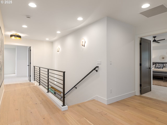 hallway with an upstairs landing, recessed lighting, and light wood-type flooring