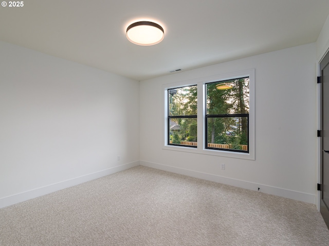 empty room with baseboards, visible vents, and light carpet