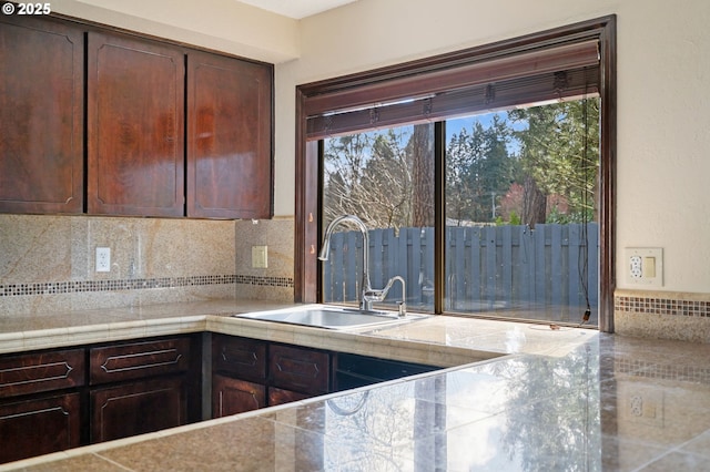 kitchen with a sink, backsplash, dark brown cabinets, and light countertops