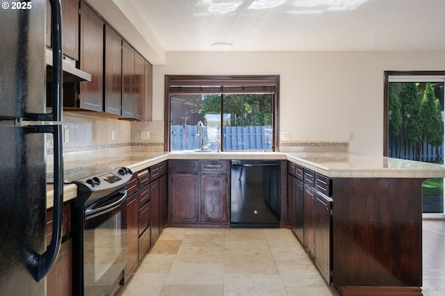 kitchen with under cabinet range hood, black appliances, a peninsula, and light countertops