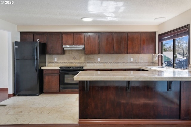 kitchen featuring a sink, decorative backsplash, black appliances, light countertops, and under cabinet range hood